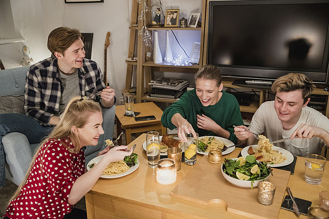 Junge Leute essen gemeinsam am Wohnzimmertisch Spagetthi